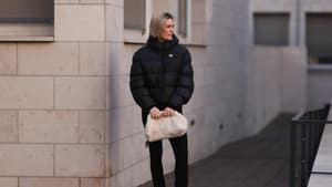 Frau trägt Puffer Jacke schwarz Hose in Schwarz beige Tasche