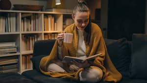 Frau mit einer gelben Decke liest ein Buch auf der Couch