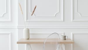 Weiße Vase steht auf einem Holzschreibtisch vor einer weißen Wand