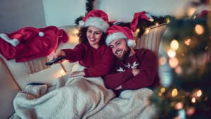 Paar mit Weihnachtsmützen sitzt unter einer Decke auf der Couch