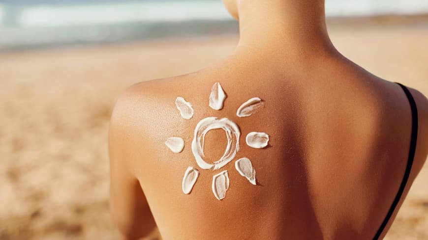 Frau sitzt am Strand mit Sonnencreme auf dem Rücken