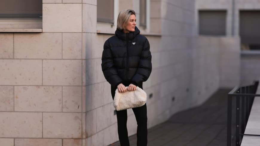 Frau trägt Puffer Jacke schwarz Hose in Schwarz beige Tasche
