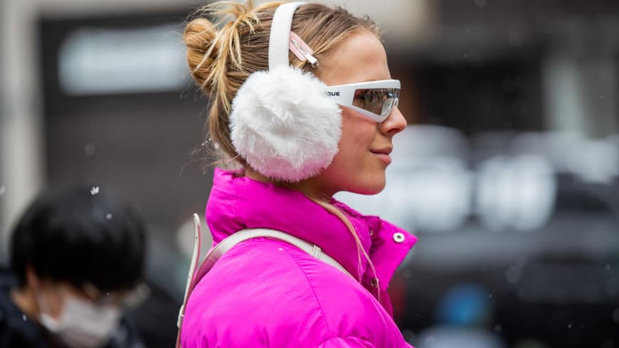 Frau trägt weiße Ohrenschützer mit Sonnenbrille pinker Jacke