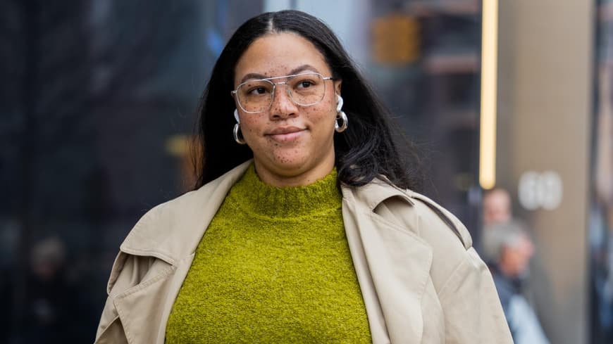 Eine curvy Frau trägt einen gelben Rock, einen Trenchcoat und einen grünen Pullover