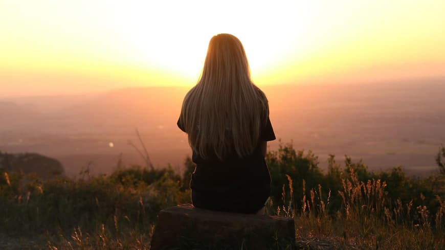 Frau sitzt auf einem Hügel und blickt in den Sonnenuntergang