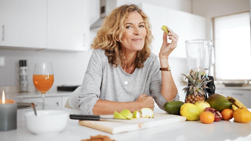 Frau ab 50 isst Obst in der Küche