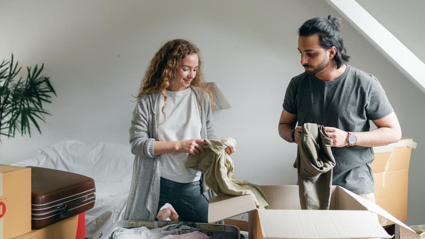 Paar steht vor einer Kiste und sortiert Kleidung aus