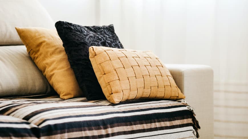 Schwarze und gelbe Kissen liegen auf einem beigefarbenen Sofa