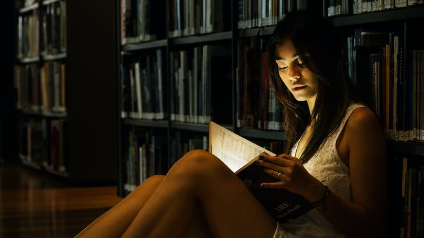 Frau im Kleid liest ein Buch in einer Bibliothek