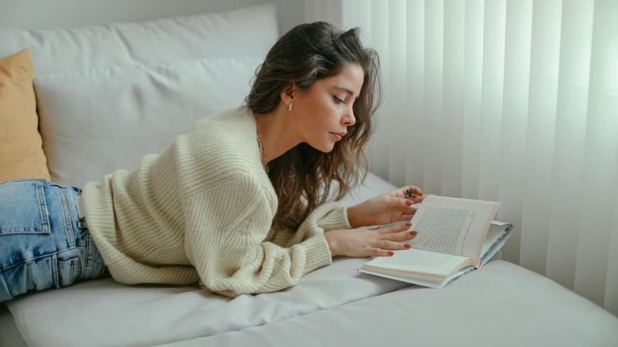 Frau mit lockigen Haaren liest eni Buch auf dem Sofa