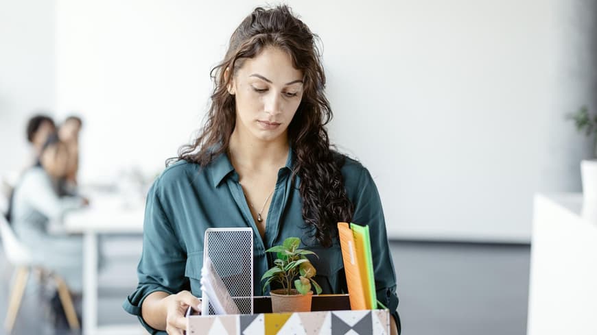 Frau steht nach einer Kündigung mit einem Karton im Büro