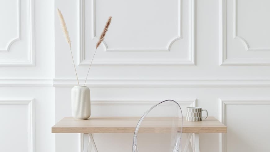 Weiße Vase steht auf einem Holzschreibtisch vor einer weißen Wand