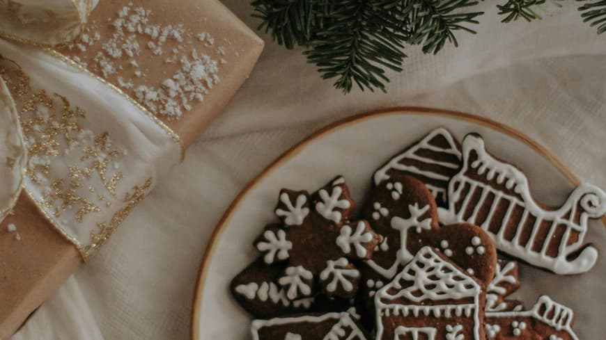 Teller mit Weihnachtsplätzchen steht neben einem Geschenk und einem Bund Tanne