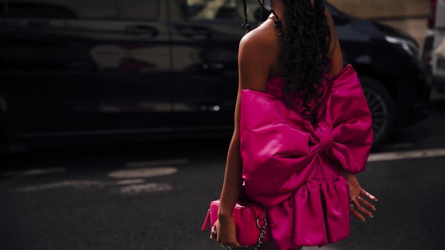Frau trägt auf Paris Fashion Week pinkfarbenes Kleid mit Schleife und passender Tasche in der Hand