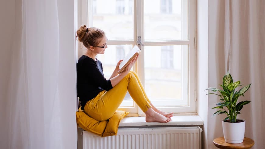 Frau liest ein Buch auf der Fensterbank