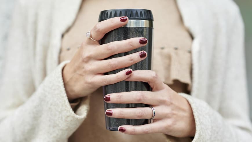 Frau hält einen Thermobecher in der Hand.