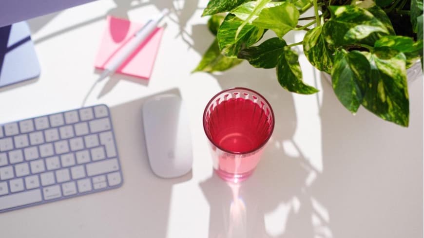 Auf einem Schreibtisch steht ein Glas und ein Computer