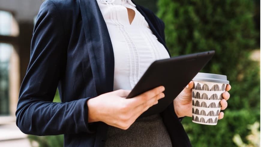 Eine Frau mit iPad und Kaffeebecher in der Hand