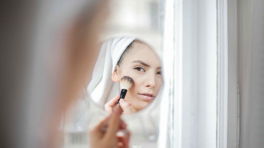 Frau mit Make-up Pinsel schaut in den Spiegel