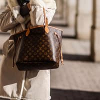 Frau in beigefarbenem Mantel mit Louis Vuitton Tasche