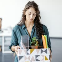 Frau steht nach einer Kündigung mit einem Karton im Büro