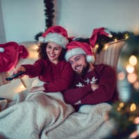 Paar mit Weihnachtsmützen sitzt unter einer Decke auf der Couch
