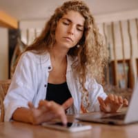Frau sitzt mit Laptop und Handy am Schreibtisch