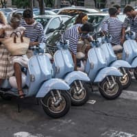 Typische Szene vor hellblauen Rollern mit Italienerinnen und Italienern