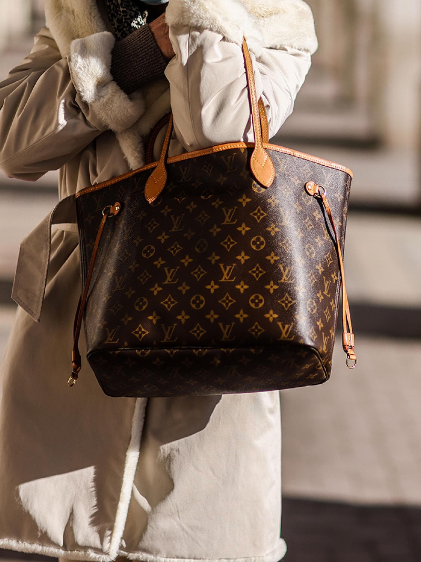 Frau in beigefarbenem Mantel mit Louis Vuitton Tasche
