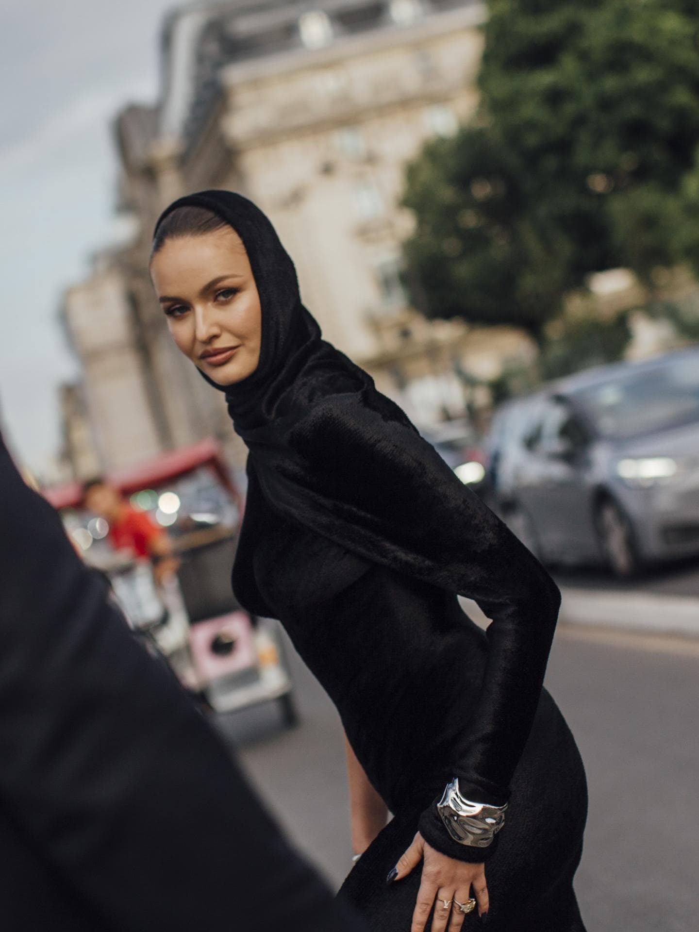 Paris Fashion Week Streetstyle Frau trägt schwarzes Kleid mit Kapuze