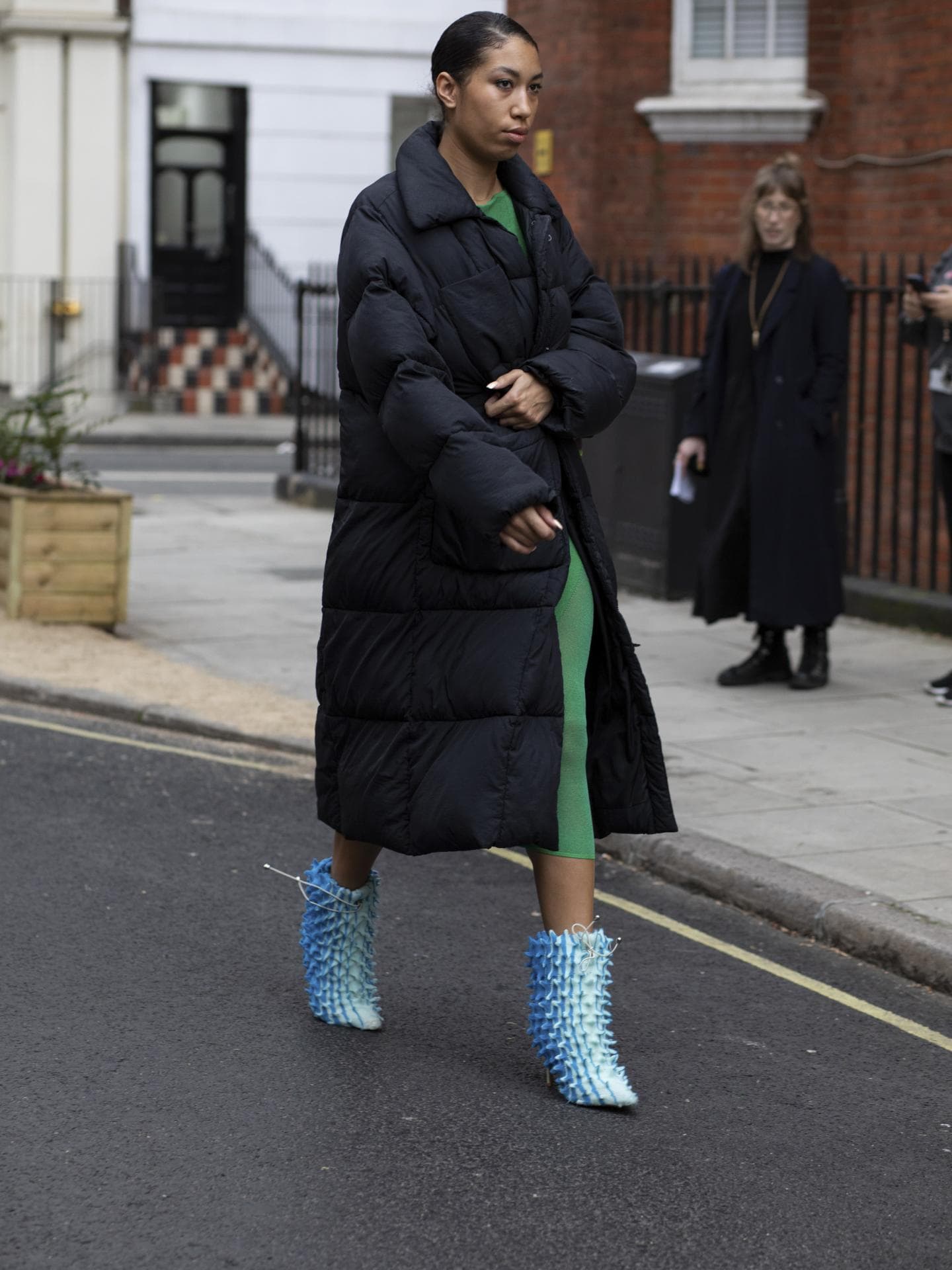 Frau trägt auf London Fashion Week schwarzen wattierten Mantel mit Stiefeletten