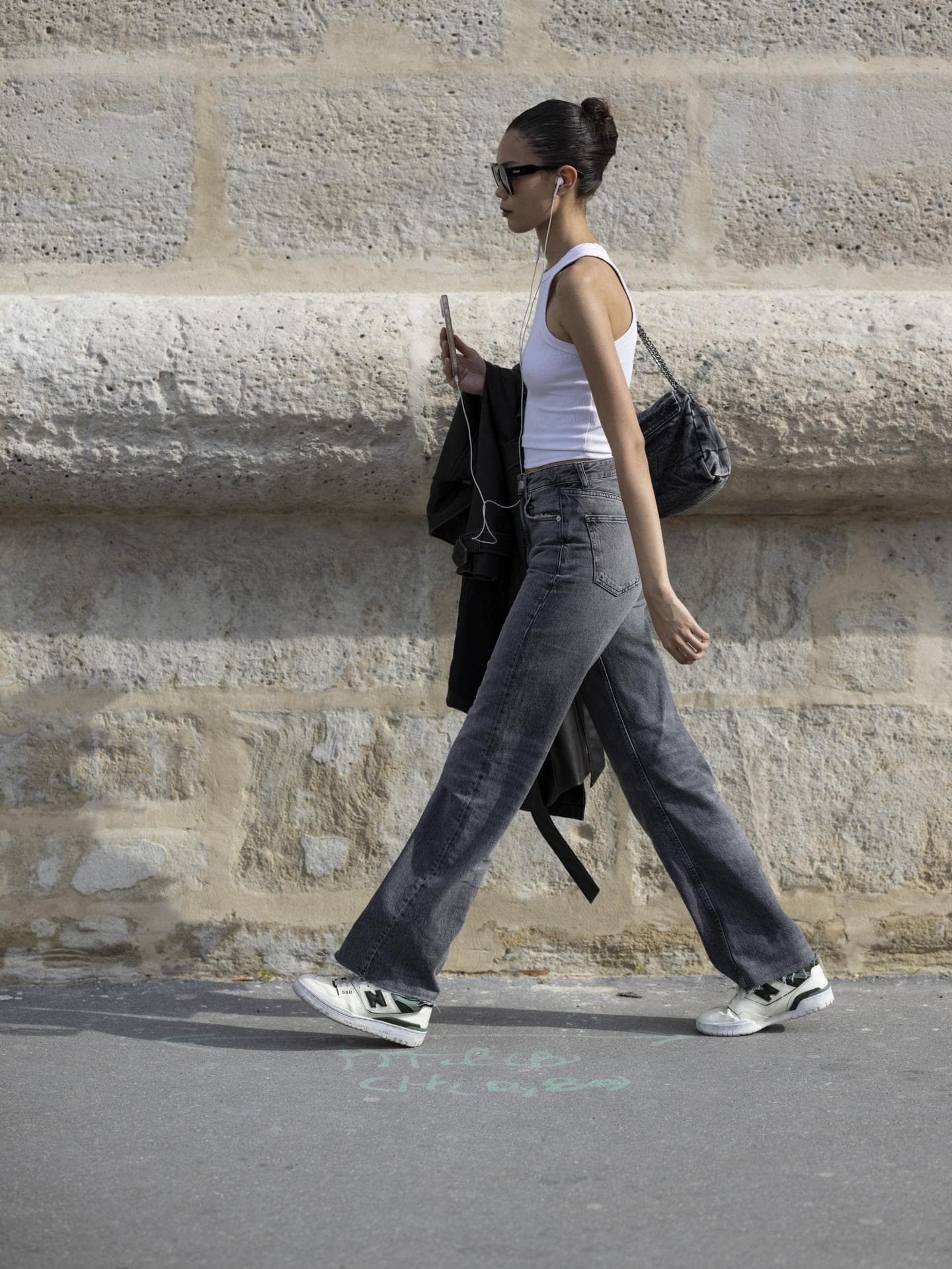 Frau trägt auf Paris Fashion Week Jeans in Grau mit Sneakern und Top Streetstyle