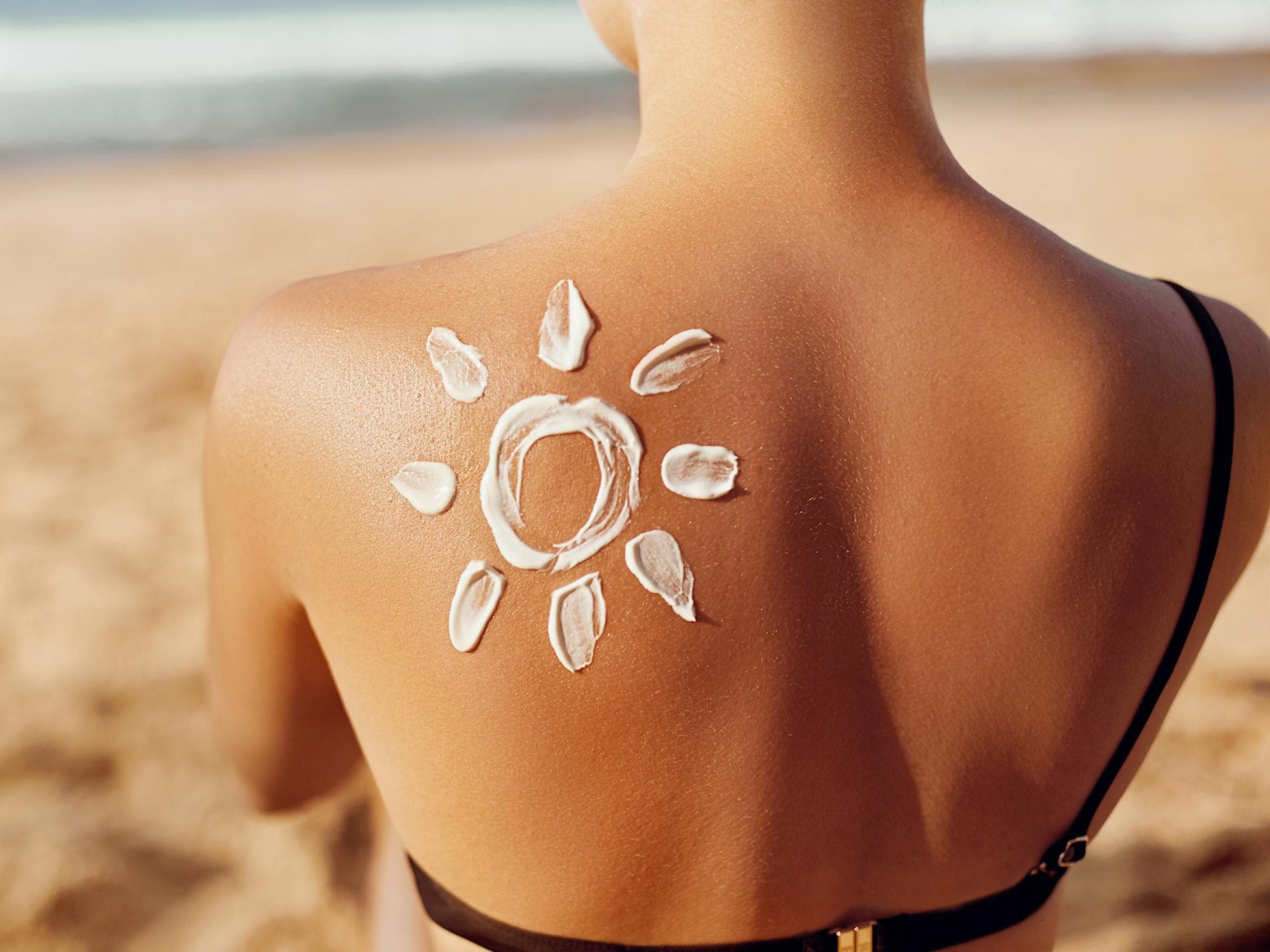 Frau sitzt am Strand mit Sonnencreme auf dem Rücken