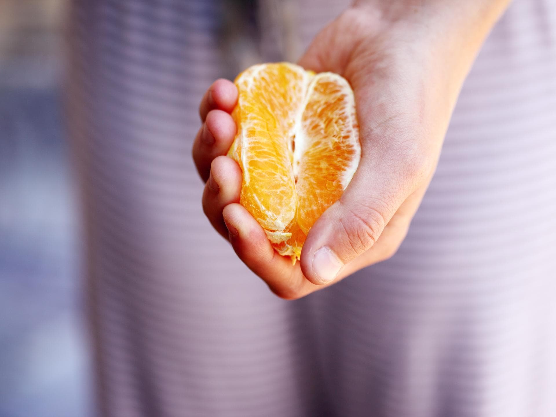 Hand mit Mandarine in der Hand Hälfte davon geschält