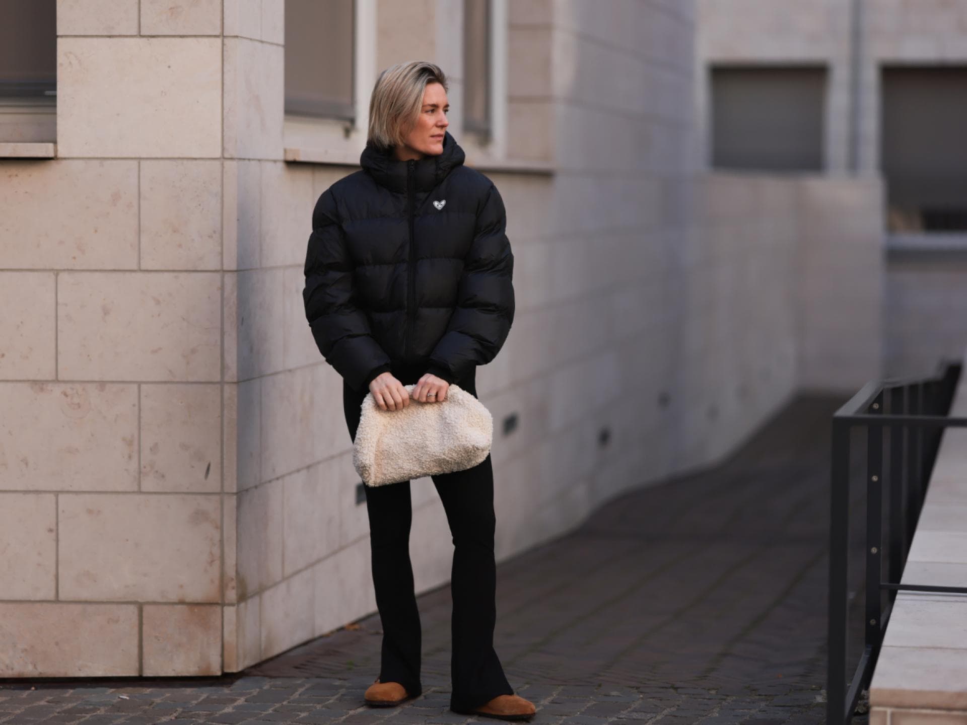 Frau trägt Puffer Jacke schwarz Hose in Schwarz beige Tasche