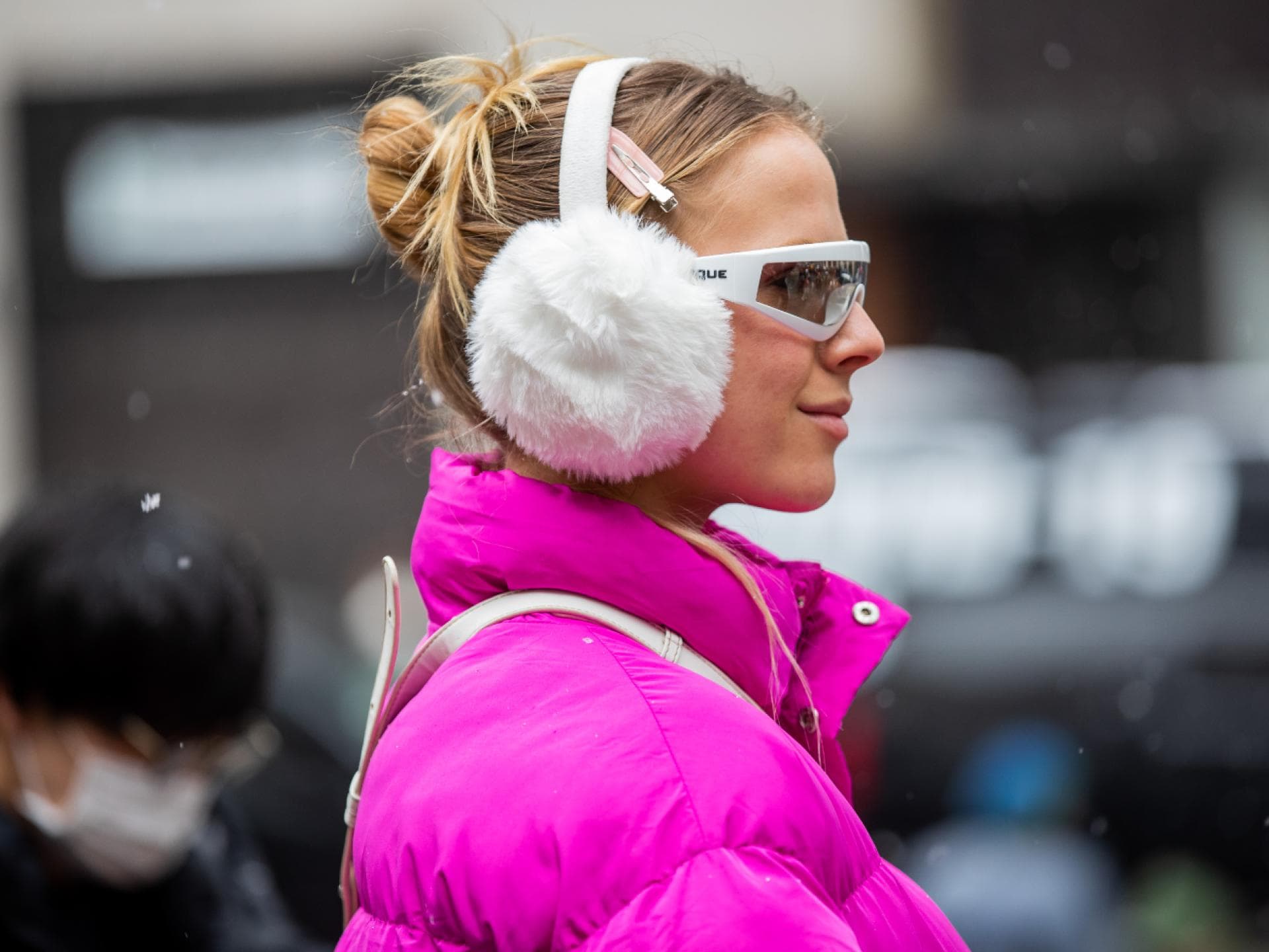 Frau trägt weiße Ohrenschützer mit Sonnenbrille pinker Jacke