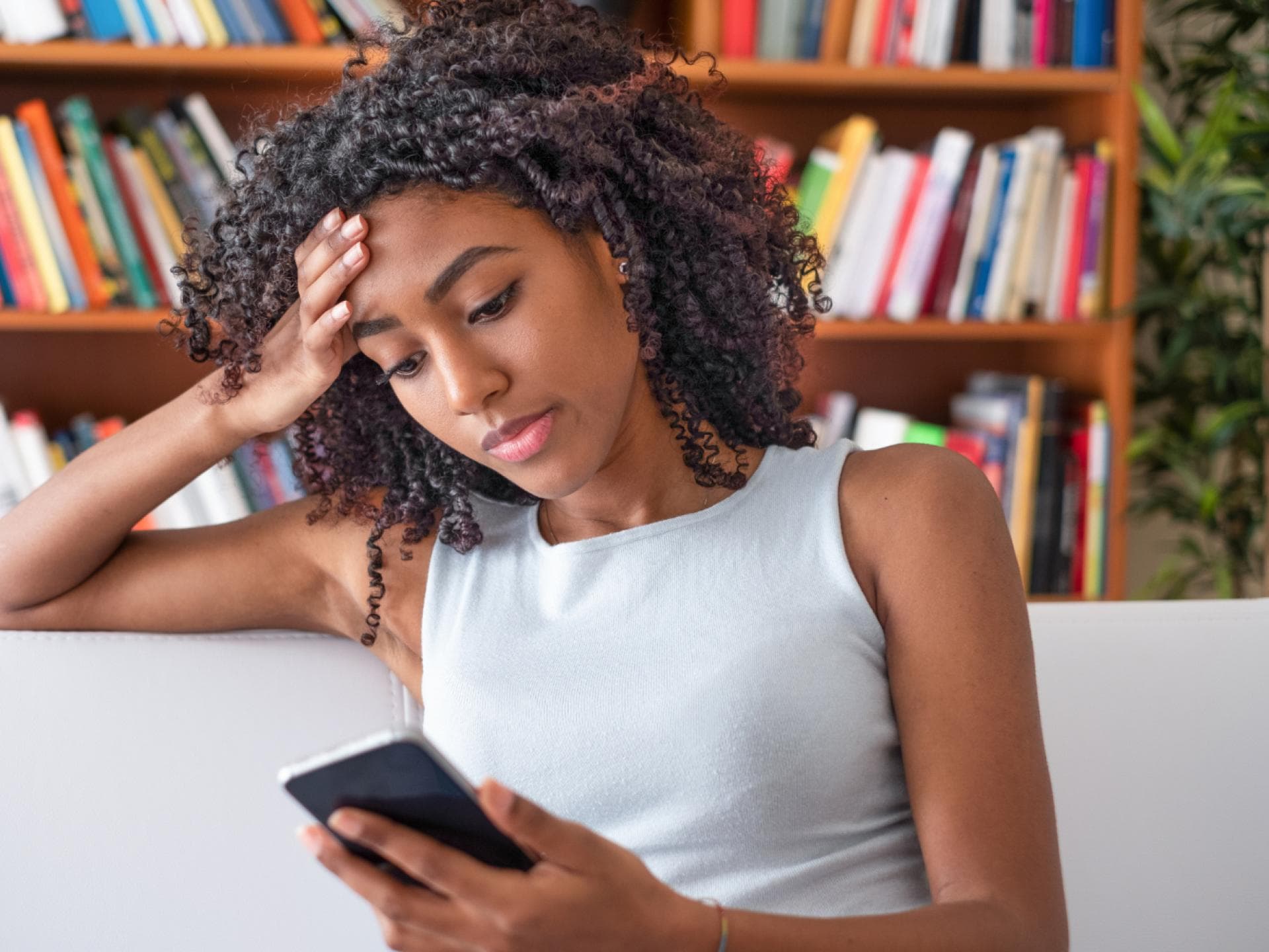 Frau hält Handy zu Hause in der Hand auf dem Sofa