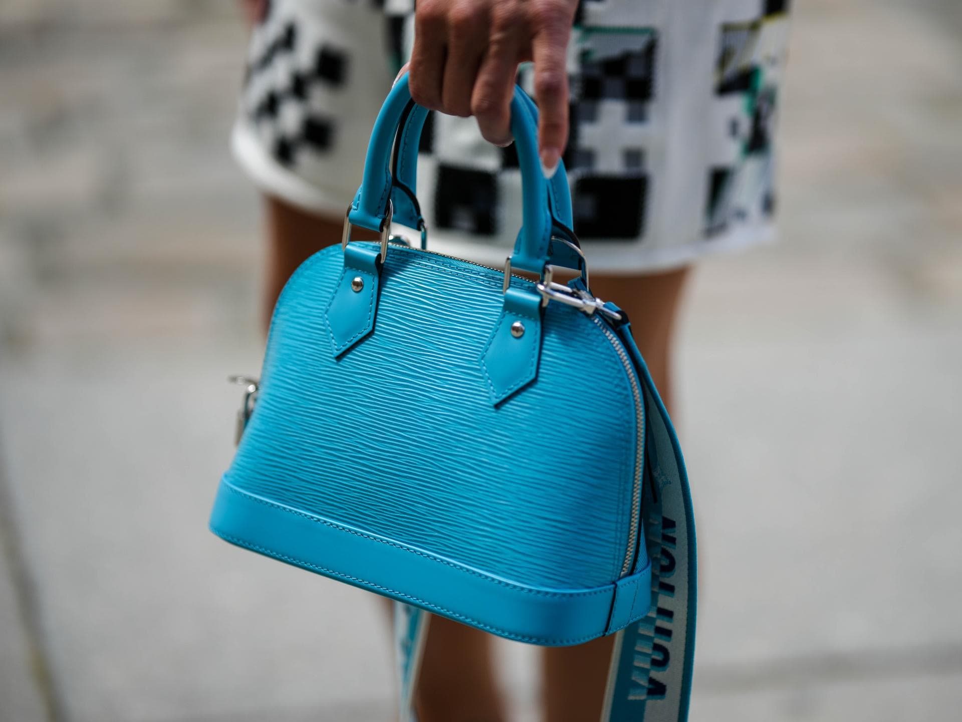 Eine Frau trägt eine türkisfarbene Louis Vuitton Alma Tasche