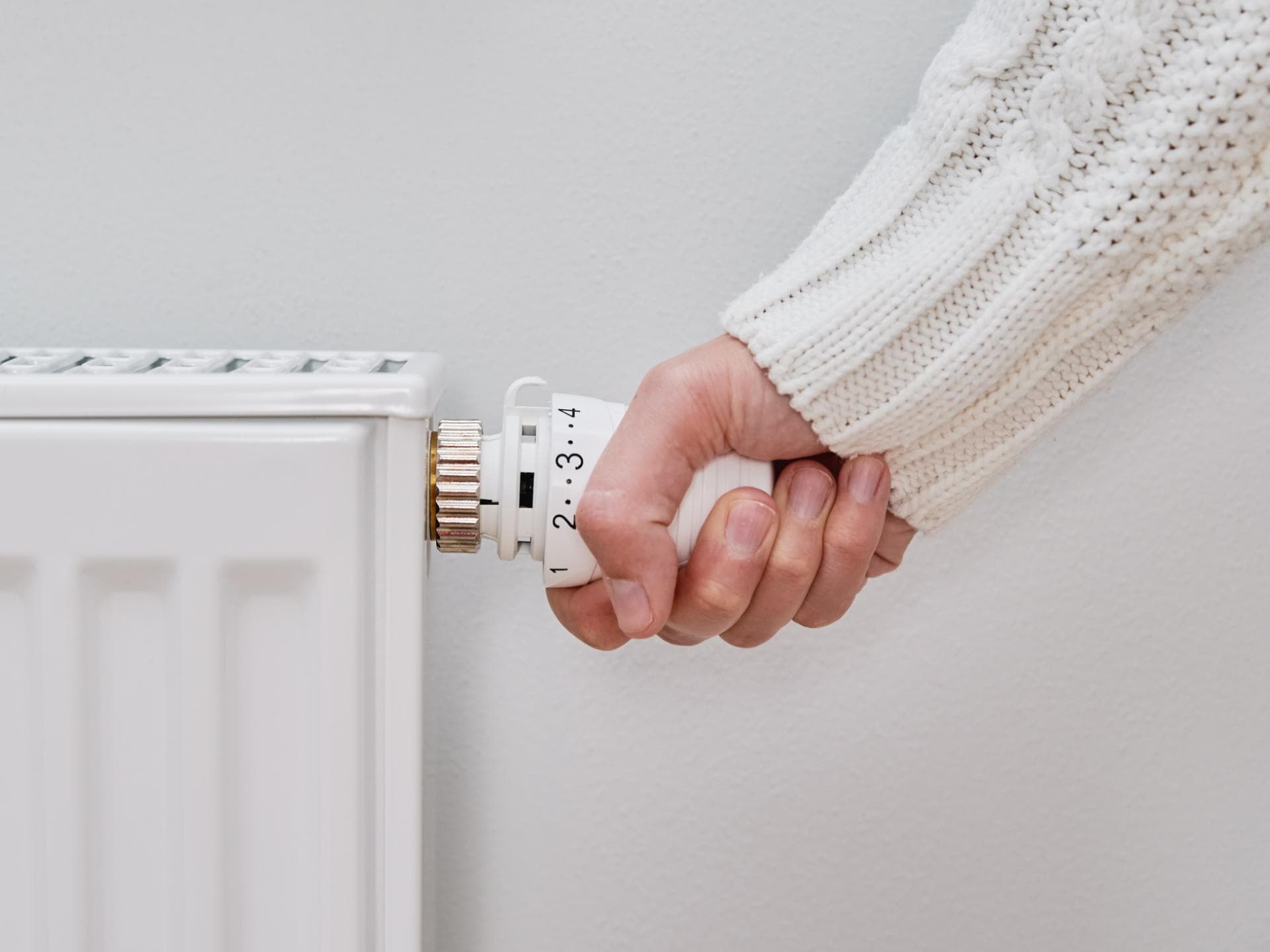 Frau im weißen Pullover dreht die Heizung auf