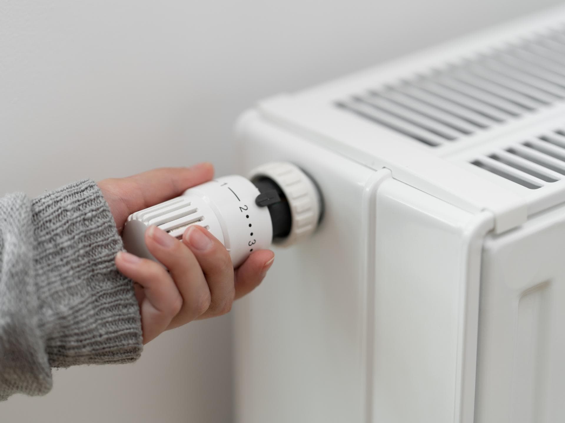 Frau im grauen Pullover dreht die Heizung auf