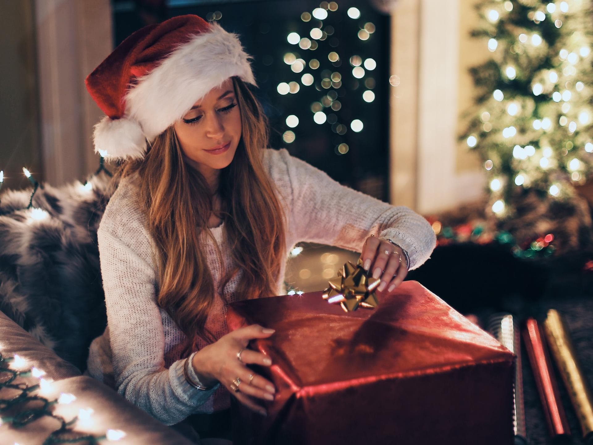 Weihnachten alleine Frau mit Weihnachtsmütze packt ein Geschenk auf dem Sofa ein