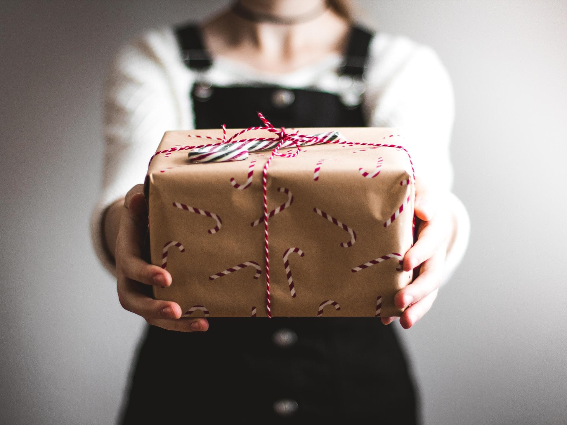 Weihnachtsgeschenk umtauschen Frau im schwarzen Latzkleid hält ein verpacktes Geschenk in die Kamera