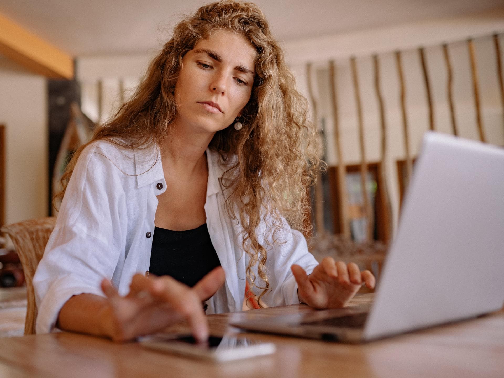 Frau sitzt mit Laptop und Handy am Schreibtisch