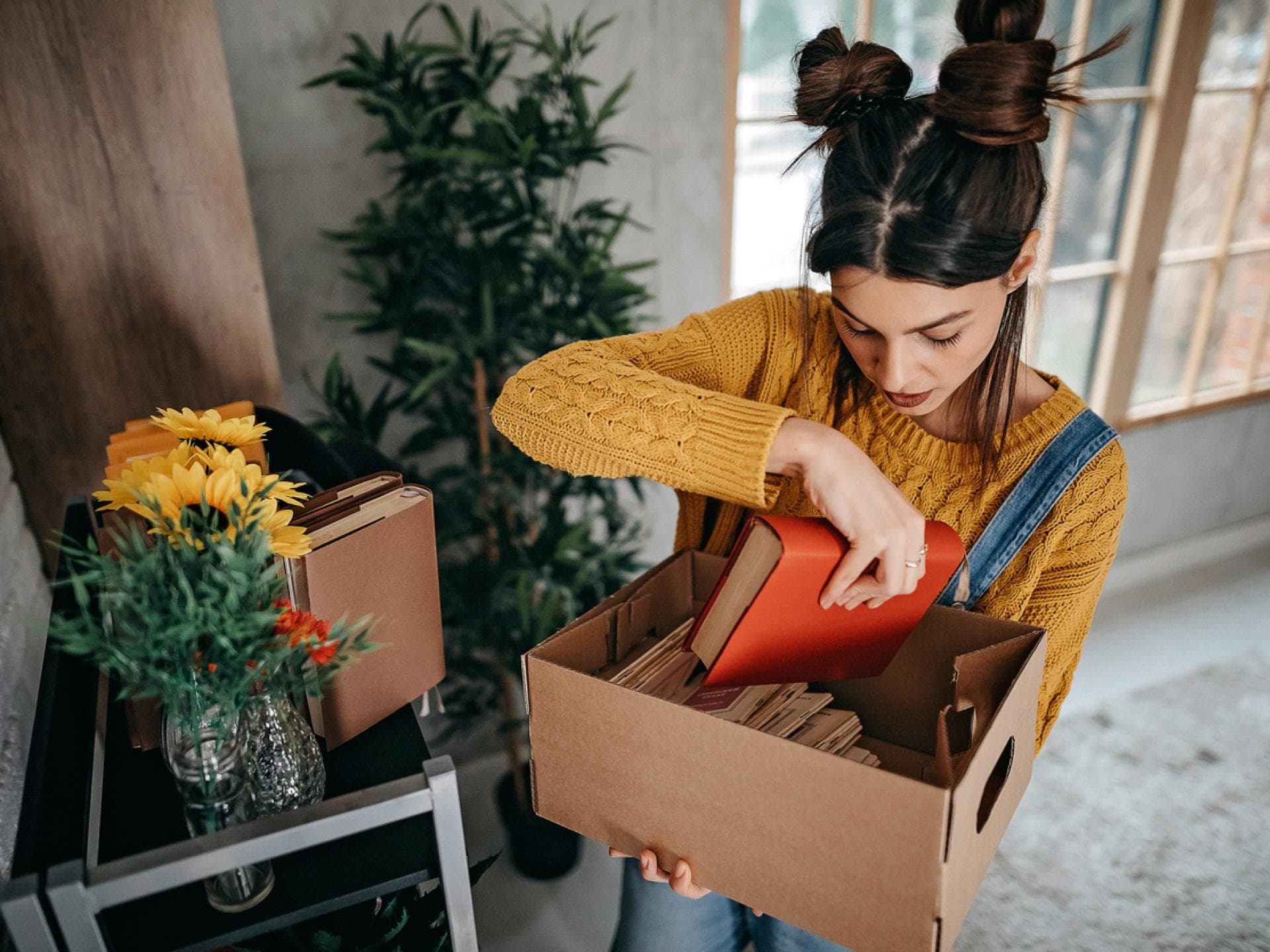 Frau legt ein rotes Buch in eine Kiste aus Pappe 