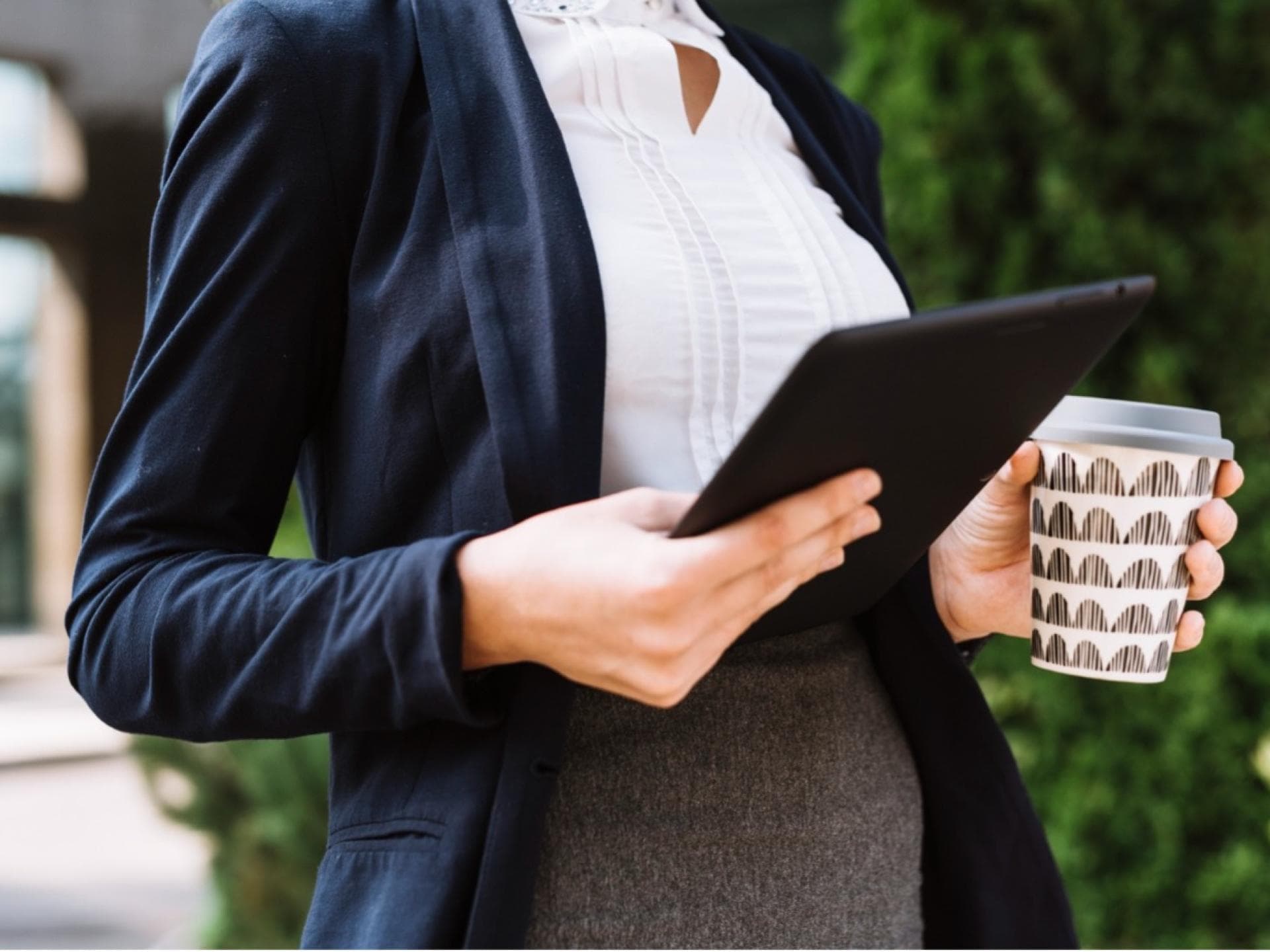 Eine Frau mit iPad und Kaffeebecher in der Hand