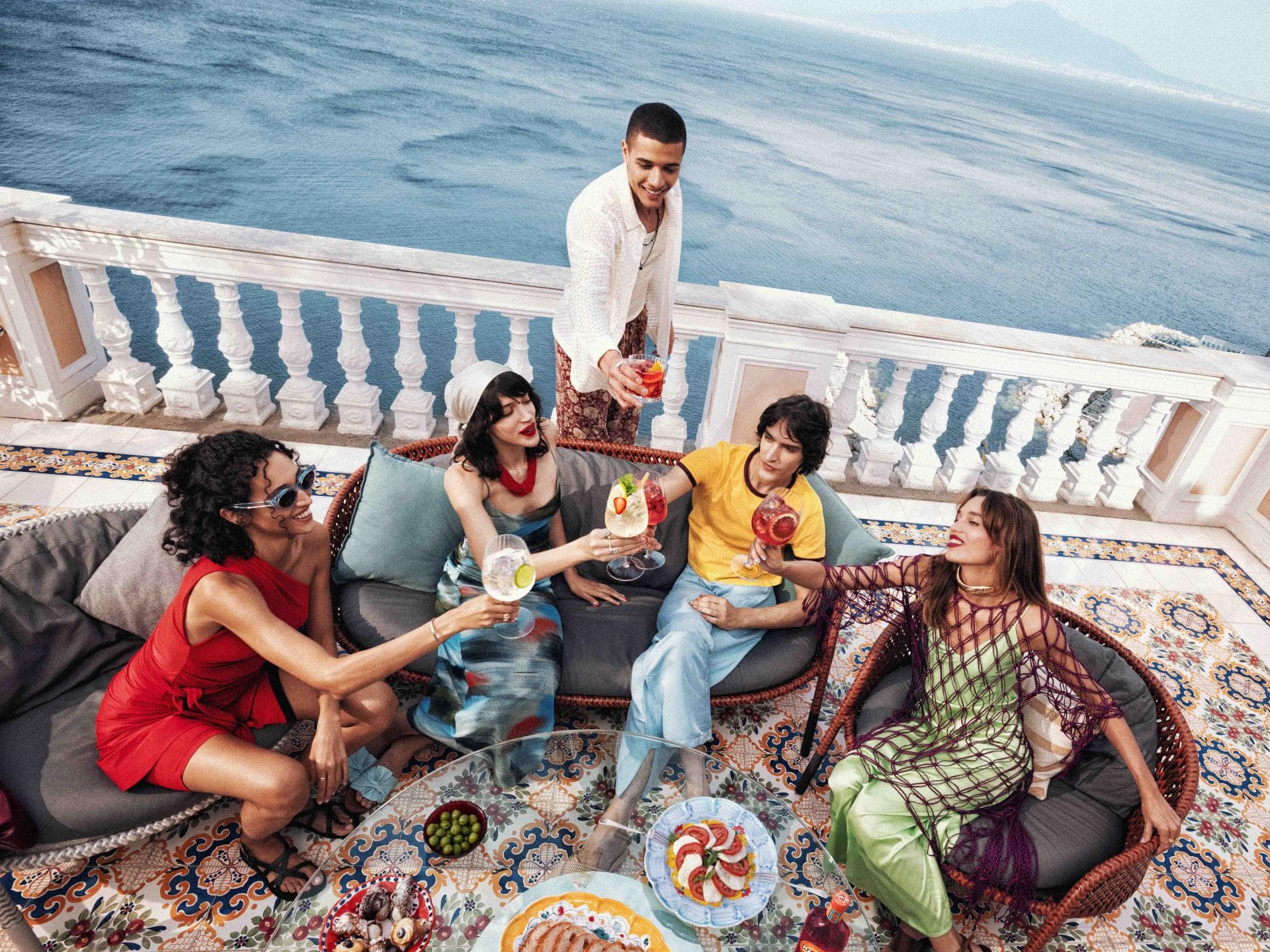 Aperitivo im Sommer mit Freunden auf italienischer Terrasse am Meer Freunde genießen gemeinsam einen italienischen Aperitivo auf einer Terrasse mit Meerblick und bunten Cocktails bei Sonnenuntergang.