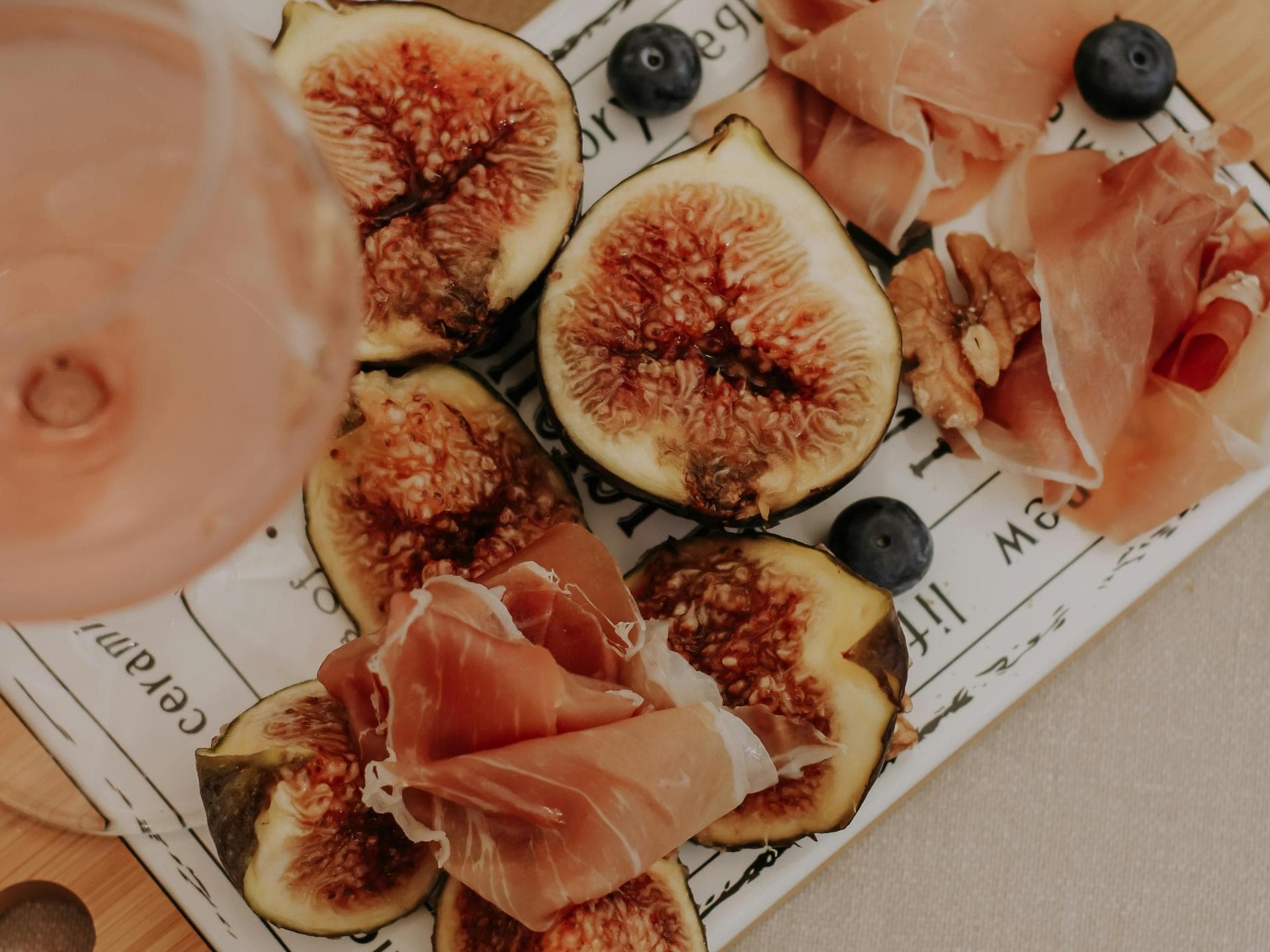 Sommerlicher Aperitivo mit Feigen, Prosciutto und italienischen Snacks Feigen, Prosciutto und frische Snacks liegen auf einer Servierplatte neben einem sommerlichen Aperitivo-Getränk.