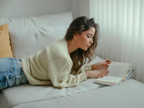 Frau mit lockigen Haaren liest eni Buch auf dem Sofa