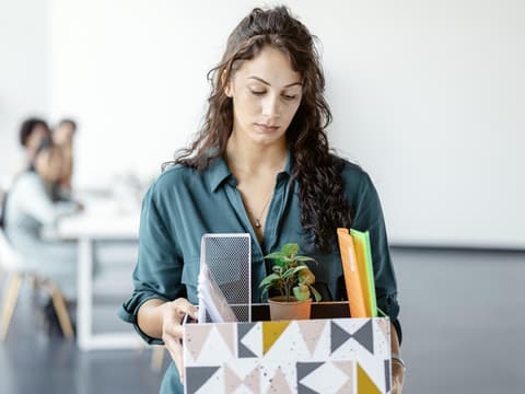 Frau steht nach einer Kündigung mit einem Karton im Büro