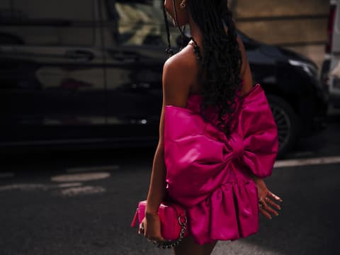 Frau trägt auf Paris Fashion Week pinkfarbenes Kleid mit Schleife und passender Tasche in der Hand